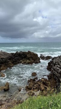 Atlantic coastal cliffs and rocky inlet beneath changing skies on the Costa Quebrada coast, with ocean water flowing through the rocks.