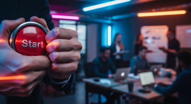 Hands press large red 'Start' button in modern tech office, symbolizing innovation and business launch