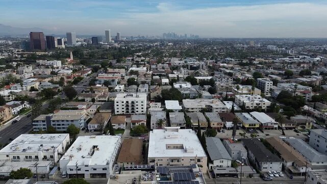 Blocks east of S Robertson Blvd extend toward Downtown Los Angeles skyline with dense housing midrise clusters. Varied roof tones, layered greenery, soft haze shape elevated perspective in CA