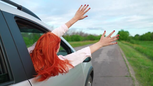 Young girl with red hair catches wind from car window. Beautiful female student drives car on way to dream. Family trip, teenage girl traveling by car. Family vacation. People traveling. Travel car