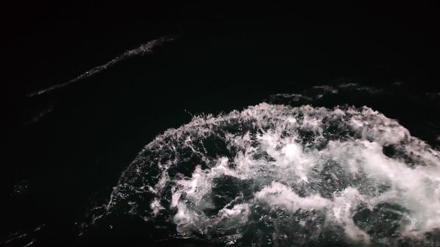 High angle slow motion shot of splashing sea waves and white water foam generated by a boat propeller engine in the dark ocean, abstract maritime background texture