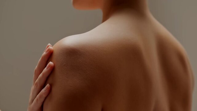 Close-up of bare back shoulder. Hand gently touches skin. Soft lighting highlights smooth skin texture. Calm, soothing, and relaxed atmosphere. Ideal for wellness, massage, or self-care themes