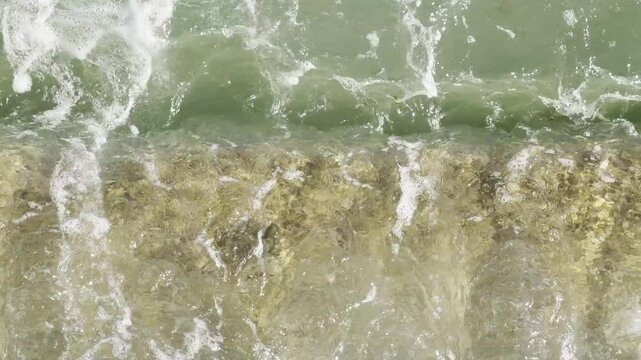 Green sea water splashing on stone detail