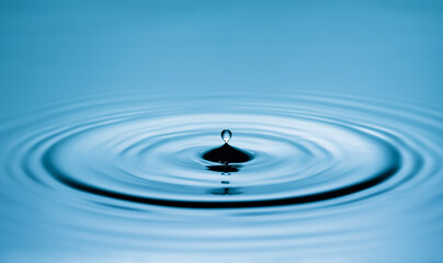 Close up of a blue water drop macro creating concentric ripples on a calm water surface. Abstract liquid background symbolizing purity, freshness, balance and clean water © Marykor
