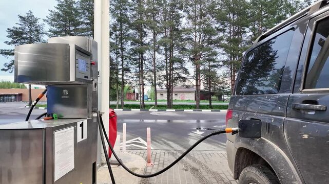 footage of a vehicle being refueled at a fuel station. Fuel hose is connected to the open fuel tank while numbers change on the pump display during the filling process. Practical transportation and