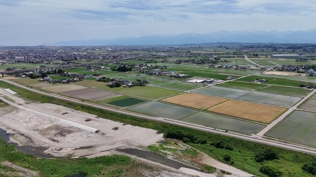 Aerial view of neat farmland and village. Fields divide into geometric shapes. Roads and paths connect rural areas. Distant hills frame the horizon. No people visible in this shot