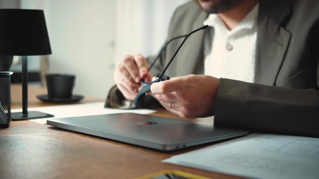 Video of an anonymous architect cleaning his glasses and starting his workday with architectural plans and a laptop. Architecture and professional workflow concept.
