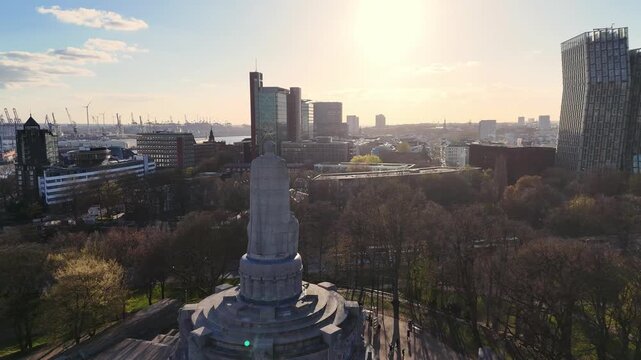 Hamburg, Germany - 30 May 2026: Aerial view of the Bismarck Monument surrounded by lush trees with the city skyline and harbor in the background during sunset.