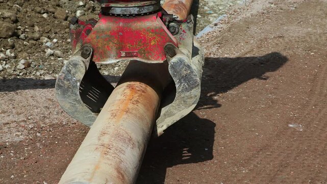Excavator Grapple Handling Large Steel Pipe at Construction Site