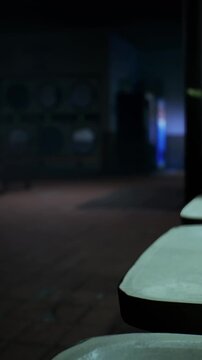 A row of empty chairs is visible in a dark room. The lighting creates shadows and depth. The atmosphere suggests the space is quiet. The floor is bare, adding to the mood of stillness.