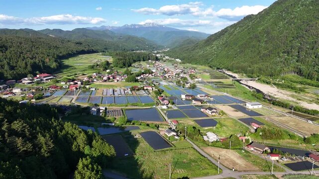 Lush green mountains frame tranquil village below. Rows of solar panels reflect the clear blue sky. Villagers live peacefully in this scenic valley