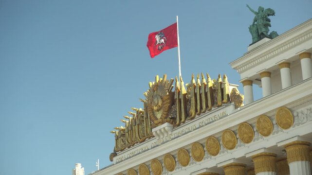 Ornate historic building facade with flag, crest, and rooftop statue against a clear blue sky. Ussr