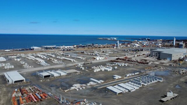 Drone footage flying over the port and industrial waterfront of Matane, showcasing a concrete mixing facility beside the St. Lawrence River under clear skies.
