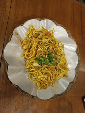 Delicious Indonesian bakmi goreng or fried noodles topped with fried shallots and celery. Authentic Asian street food flat lay on a rustic wooden background, perfect for menus.