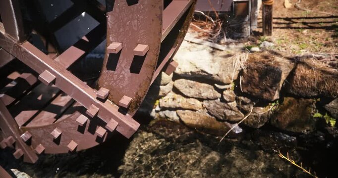 Water falling on watermill and making it spin - tilt shot