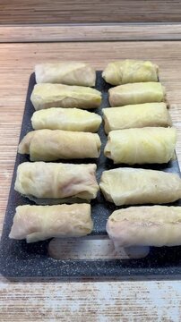 Cabbage rolls on black cutting board closeup, uncooked meat filled cabbage leaves rolled into neat cylinders, arranged in rows