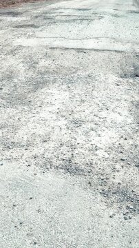 Gravel road pothole damage daytime closeup of rutted asphalt and scattered rubble showing cracked surface texture, uneven patches
