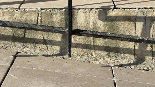 Porch entrance with new tiles, sunlit concrete steps and black metal railing casting long shadows, textured masonry riser