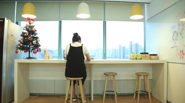 사람 프리랜서 업무 노트북 작업 오피스 인테리어 창가 소품 디테일 자재: 실내 공유오피스 창가 바테이블에서 화이트보드와 트리를 배경으로 작업하는 인물의 뒷모습을 포착한 풀숏입니다.
