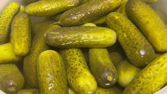 Fresh market pickles in container, closeup of clear plastic tub packed with brined cucumbers, glistening brine