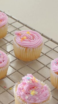 Vertical video: Panning lens centering cupcake on counter, pink rosette pastel stars on rack