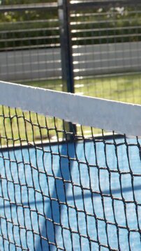 Vertical video: Panning camera revealing blue court net and post, showing fence and shadows
