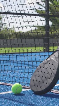 Vertical video: Entering ball rolling on blue court to net settling near padel racket, copy space