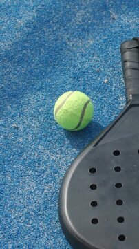 Vertical video: Rolling neon tennis ball nudging from camera move on blue court beside black paddle