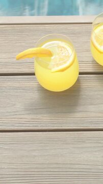 Vertical video: Drifting camera revealing stemless glass on wood table at pool edge, citrus wedge