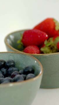 Vertical video: Drifting camera pulling focus on bowls with berries on table showing water drops