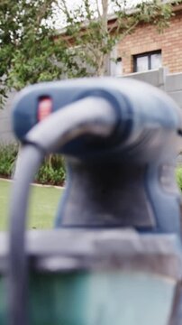 Vertical video: Hand bringing blue sander sliding across bench in backyard, preparing to sand plank