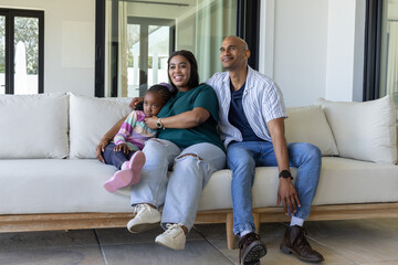 Obraz premium African American family sitting on light sofa in living room with preschool child, wristwatches