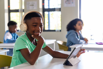 Diverse classmates with African American boy smiling, using tablet at school with beige headphones © wavebreak3