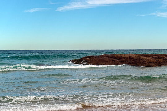 Waves Rolling Over Rocky Coastal Ledge Under Clear Blue Sky