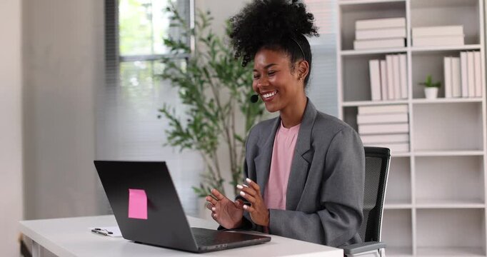 African american businesswoman smiling, wearing a headset with a microphone, providing online assistance and support while working from her home office setup