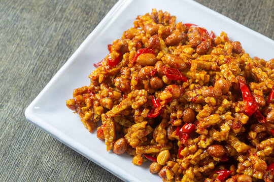 kering tempe served in white plate, Crispy caramelized tempeh strips with chili and peanuts garnish, traditional Indonesian food