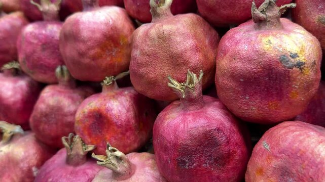 Ripe pomegranate fruits piled together, vibrant close-up of red skins and dried crowns, market stall arrangement with rustic