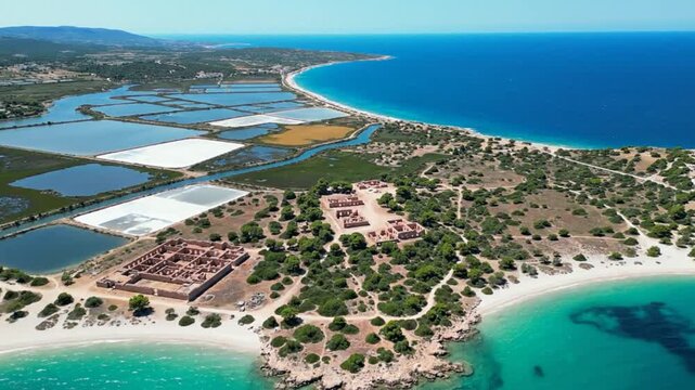 Aerial view of a coastal landscape with salt pans, ruins, and turquoise water under a sunny sky