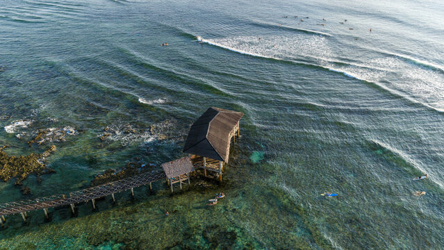Aerial view of Cloud 9 Surfing Area featuring a wooden boardwalk and pavilion over turquoise waters with surfers catching waves General Luna, Caraga, Philippines.