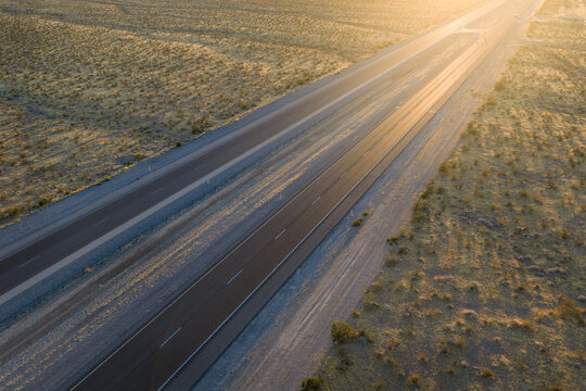 Aerial view of a long highway stretching through the arid desert landscape near Potosi Mountain during golden hour in Clark County, Nevada, United States.