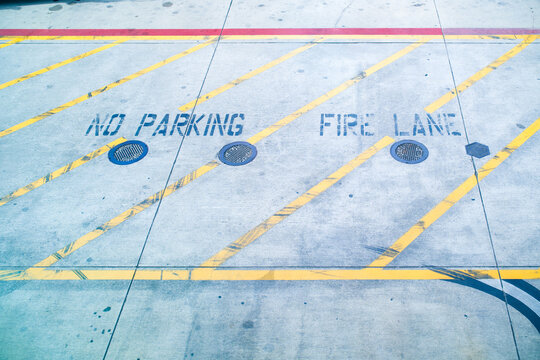 Blue words no parking fire lane and yellow diagonal lines mark concrete road pavement for emergency vehicle access restriction.