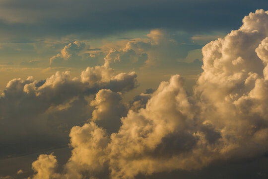 Dense massive cumulus thunderhead clouds illuminated by intense golden sunlight creating deep shadows in the evening sky.