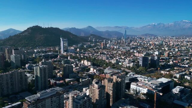 High altitude flyover above residential districts revealing full Santiago skyline with San Cristobal Hill, Costanera Center and snow-capped Andes range. Santiago, Chile
