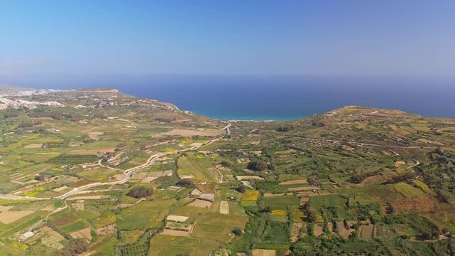 In Gozo's Ramla Bay, an aerial view shows the beach and Mediterranean shoreline bordered by terraced fields and coastal rural countryside under a clear sky.