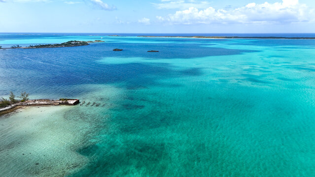 Aerial view of the vibrant turquoise waters and tropical cays under a bright blue sky with scattered clouds near George Town, Exuma, The Bahamas.