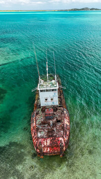 Aerial view of a rusty shipwreck in crystal clear turquoise waters showing heavy corrosion on the deck and the sandy seabed below George Town, Exuma, The Bahamas.