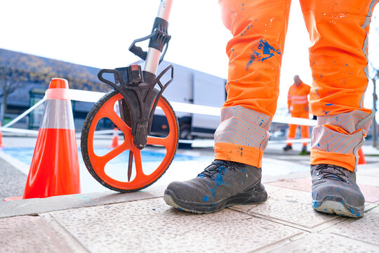 Close detail of a measuring wheel and the legs of a road worker taking measurements on asphalt during urban parking marking and signaling operations