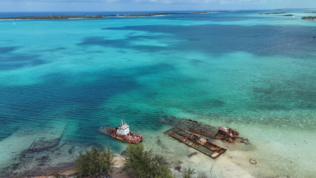 Aerial view of a rusty shipwreck and abandoned barges in the crystal clear turquoise waters along the coast of George Town, Exuma, The Bahamas.