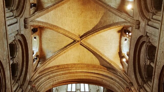 Upward interior view of grand Romanesque stone arches and vaulted cathedral ceiling illuminated with warm light inside Durham Cathedral.