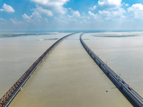 Aerial view of Jamuna Bridge and the parallel railway bridge spanning the wide Jamuna River under a blue sky in Tangail District, Dhaka Division, Bangladesh.